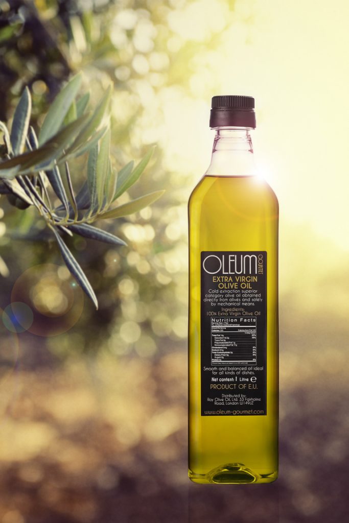 Botella de aceite virgen extra OLEUM en un olivar al atardecer. El sol acentúa su transparencia. Fotografía publicitaria de producto realizada para una fábrica de aceite.